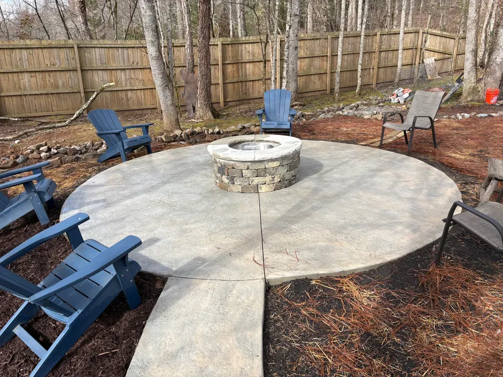 Round concrete patio with a stone fire pit and chairs